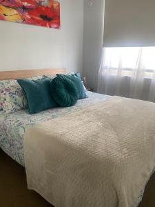 Un dormitorio con una cama con almohadas azules y una ventana en Bonito y acogedor departamento en Los Ángeles