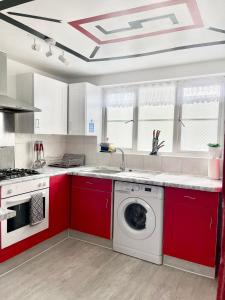 uma cozinha com armários vermelhos e uma máquina de lavar roupa em Westfield Gardens Apartment - 3 bedrooms em Goodmayes