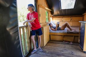 Un uomo in piedi in una cabina con una donna sdraiata sul letto di Les Auzerals camping du lac a Rabastens