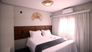 um quarto com uma cama com lençóis brancos e uma janela em Pousada Encantos do Coqueiro em Luis Correia