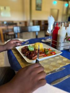 eine Person, die ein Messer und einen Teller Essen hält in der Unterkunft Hotel Tum's Water World in Manzini
