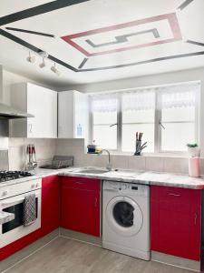 Westfield Grove 3 Bedroom Apartment في Goodmayes: مطبخ مع دواليب حمراء وغسالة ملابس