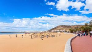 a beach with umbrellas and people walking on the sand at Appartement en résidence avec piscine in Agadir