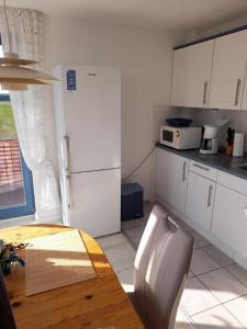 a kitchen with a table and a white refrigerator at Moderne Ferienwohnung mit Balkon in Strandnähe in Friedrichskoog
