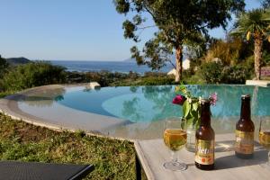 two bottles of wine and glasses on a table near a swimming pool at studio, vue sur mer et montagne in Saint-Florent