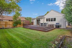 a backyard with a white house with a wooden deck at Prosper Point Home with BBQ, Patio and Parking in Auckland