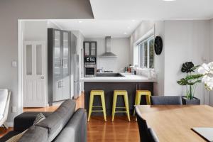 a kitchen and living room with a couch and yellow stools at Prosper Point Home with BBQ, Patio and Parking in Auckland