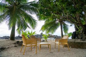 4 Stühle und ein Tisch am Strand mit Palmen in der Unterkunft LE ROCHER DE TAHITI in Mariuti