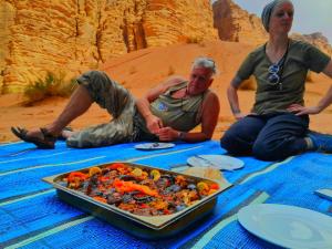 three people sitting on a blanket with a tray of food at Lukasa camp Wadi Rum in Disah