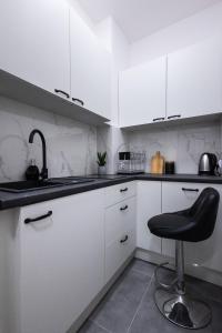 una cocina con armarios blancos y una silla negra en ClickTheFlat Wolska Apart Rooms, en Varsovia