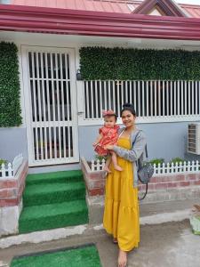 una mujer sosteniendo un bebé delante de una casa en Catrionna Doll House en Tagum