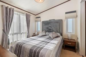 a bedroom with a bed with a large headboard and windows at Cormorant - Luxury Lodge Close to the Beach in Tenby