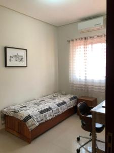 a bedroom with a bed and a desk and a window at Casa Agradável com muito espaço 