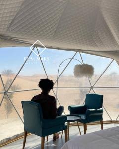 una mujer sentada en una silla mirando por una ventana en Rum Mars luxury camp, en Wadi Rum