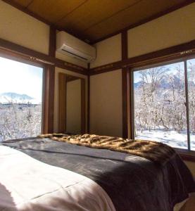 a bedroom with a bed and two large windows at Lucky Duck Cabin Myoko in Myoko
