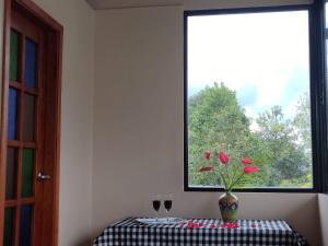 uma mesa com um vaso com flores vermelhas e uma janela em Bio-Hotel entre café, bosque y montañas em Cachipay