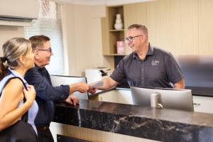 ゴールドコーストにあるSouthport Motel & Apartmentsのカウンターで女性と握手する男性2人