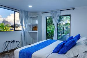 a bedroom with a bed with blue pillows and a window at Hotel Santa Maria de las Aguas Peñol in Guatapé
