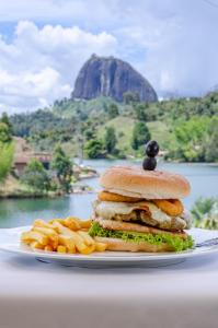 een sandwich en frietjes op een bord met een berg op de achtergrond bij Hotel Santa Maria de las Aguas Peñol in Guatapé