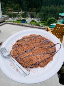 a chocolate cake on a plate with a fork and knife at Trippy Trails in Kasol