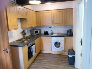 cocina con armarios de madera, lavadora y secadora en Apartment in Historic Mill, near Dover Port en Kent