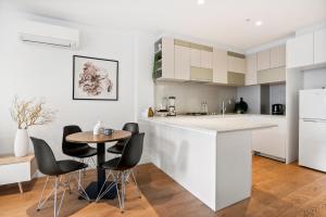 een keuken met witte kasten en een tafel en stoelen bij Skyline Treat Apt in Middle of Shopping Haven in Melbourne