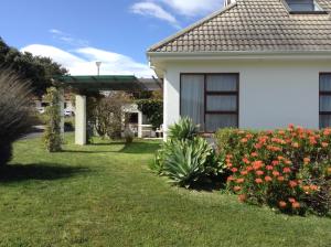 a white house with flowers in the yard at Hermanus At Rikis Self Catering in Hermanus
