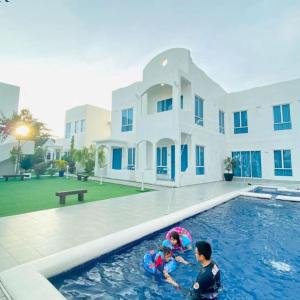 two children playing in a swimming pool in front of a house at The Arjana Resort in Masjid Tanah