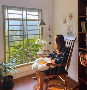 een vrouw in een schommelstoel die uit een raam kijkt bij Góc sân và Khoảng trời 2 - Đặng Thái Thân (nguyên căn) in Xuan An