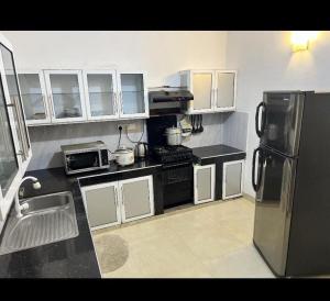 una cucina con armadietti bianchi e frigorifero nero di Araliya Uyana Apartments - Two Bed Room House a Ratmalana