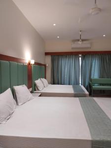 a bedroom with two beds and a bench in it at Hotel Harshanaa Elite in Kanyakumari
