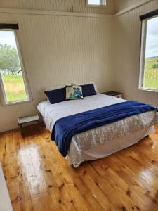 een slaapkamer met een bed met blauwe lakens en 2 ramen bij Andy's View in Lake Chrissie