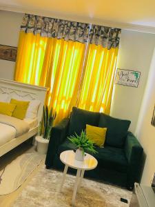 Indesign Makumbi park studio Apartment D4-5,Syokimau في Syokimau: غرفة معيشة مع أريكة خضراء وستائر صفراء