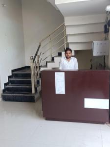 Un uomo in piedi dietro una scrivania in una stanza con le scale di Hotel JP Inn a Lucknow
