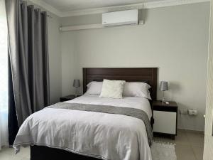 a white bedroom with a large bed and a window at Hi-Life Villa in Gaborone