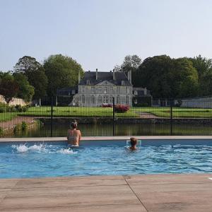 two people in a swimming pool with a house in the background at Chambres d'Hôtes Château de Martragny in Martragny