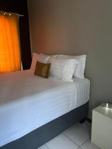 um quarto com uma cama com lençóis brancos e almofadas em Shiloh Shared em Gaborone