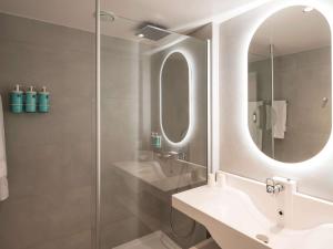 a bathroom with a sink and a shower with a mirror at Novotel Bordeaux Lac in Bordeaux