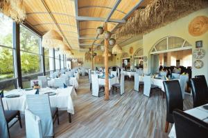 um restaurante com mesas e cadeiras brancas e janelas em Хотел и Вили Марая em Tsarevo