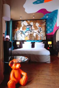 Boutique Hôtel des Beaux Arts في تولوز: غرفة نوم مع سرير ودب برتقال يجلس على الأرض
