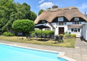 a thatched cottage with a pool in front of it at Beautiful Thatched Cottage with heated outdoor pool, Great for families & Dog Friendly! in Bosham