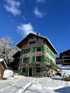 um edifício antigo com persianas verdes na neve em The Stone House - 10 Bed Chalet near Morzine em Saint-Jean-dʼAulps