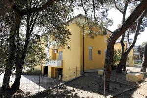 a yellow house behind a fence with trees at Villa Medea in Rosolina Mare