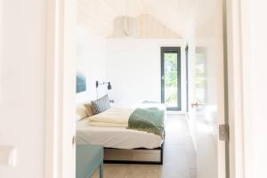 a white bedroom with a bed and a window at Fred I Tiny House op de Veluwe in Epe