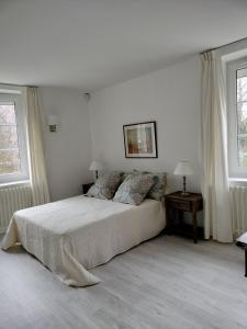 a white bedroom with a bed and two windows at Les Mulotières in Olivet