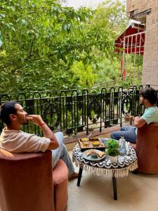 two men sitting on a porch with a table at Atharva's Homestay by Goaround Homes in New Delhi