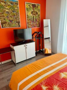 Schlafzimmer mit orangefarbenen Wänden, einem Bett und einem TV in der Unterkunft Appartamento Lignano Sabbiadoro Centro in Lignano Sabbiadoro