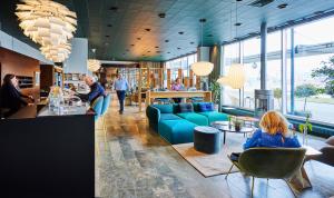 a lobby with a blue couch and people sitting in chairs at Hotel Jutlandia in Frederikshavn