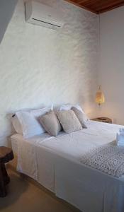 a white bedroom with a white bed with pillows at Chalé Macaúba in Santana do Riacho