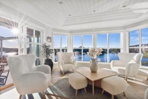 sala de estar con sillas blancas, mesa y ventanas en Waterfront Villa w/Boat&kayaks. 15min from Bergen en Foldnes